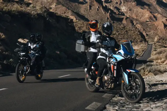 Motocykliści w kaskach jadący drogą wśród skalistych wzgórz.