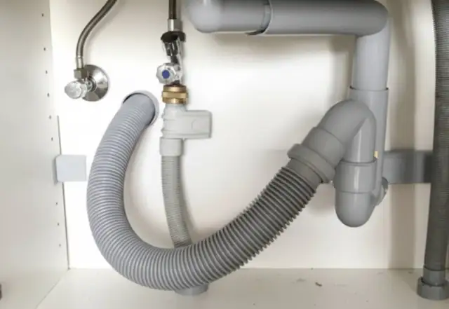 El fregadero pierde agua por abajo. Tuberías grises y mangueras flexibles bajo el lavabo, con una fuga visible.