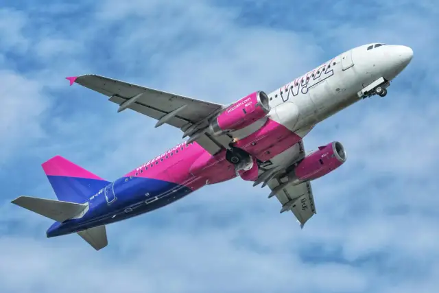 Samolot Wizz Air z różowo-niebieskim ogonem wznosi się na tle błękitnego nieba. Chcesz wiedzieć, jak przełożyć lot w Wizzair?