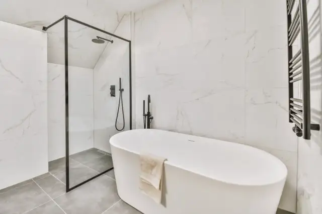Nowoczesna łazienka z wanną wolnostojącą i prysznicem. Na podłodze elegancka płytka podłogowa 60x60 w odcieniu szarości.