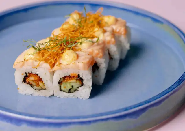 Rolka sushi z łososiem, krewetkami, ogórkiem i ikrą na niebieskim talerzu.