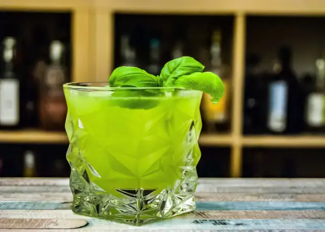 Orzeźwiający drink z likierem miętowym, ozdobiony listkami bazylii, w szklance o geometrycznym kształcie.