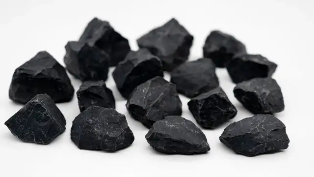 Eine Gruppe von scharfkantigen, schwarzen Steinen liegt auf weißem Grund. Die schwarzer Stein Bedeutung wird oft mit Schutz und Erdung assoziiert.