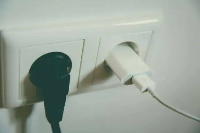 Czarna wtyczka i biała ładowarka w gniazdku elektrycznym. Bezpieczne uziemienie dla urządzeń.