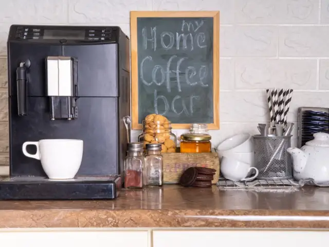 Máquina de café, taza, galletas y un letrero de "my Home Coffee bar" en un rincón de la cocina.