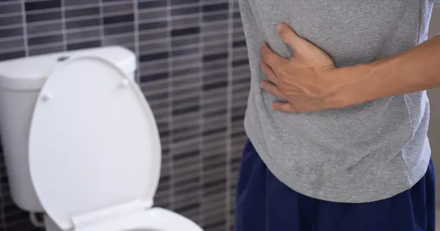 Mężczyzna trzyma się za brzuch, siedząc obok toalety. Może to być jeden z objawów raka odbytu.