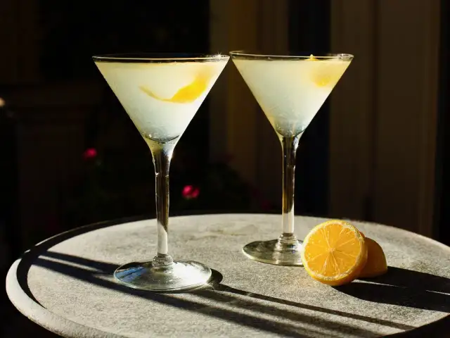 Dwa drinki z wódką waniliową i cytryną, podane w kieliszkach martini na kamiennym stoliku.