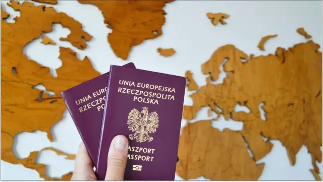 Dwa polskie paszporty, w tym paszport tymczasowy dla dziecka, na tle drewnianej mapy Europy.