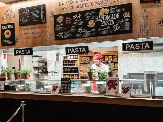 W Vapiano kucharz przygotowuje ręcznie robiony makaron. Na ścianie menu z różnymi rodzajami pasty.