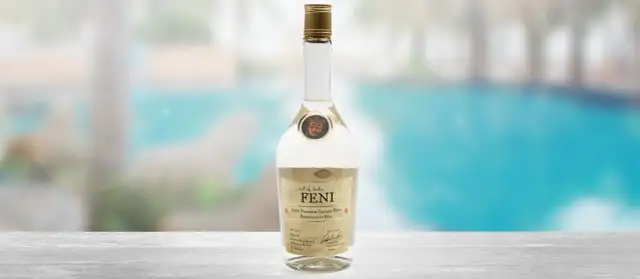 Butelka Feni, indyjskiego alkoholu z nerkowców, na tle basenu.