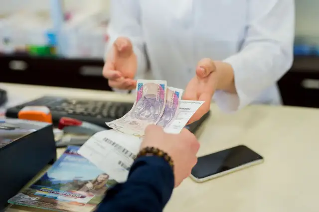 Dłoń podaje farmaceucie polskie banknoty i receptę.