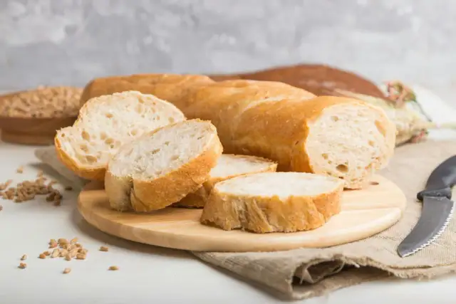 Aufgeschnittenes Baguette auf Holzbrett mit Weizenkörnern und Messer.