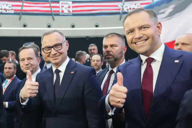 Dwóch mężczyzn w garniturach, jeden z nich pokazuje kciuk w górę. W tle widać napis CPAC Poland. Długość kadencji prezydenta jest tematem dyskusji.