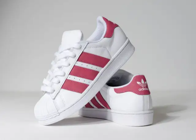 Białe buty Adidas Superstar z różowymi paskami i logo.