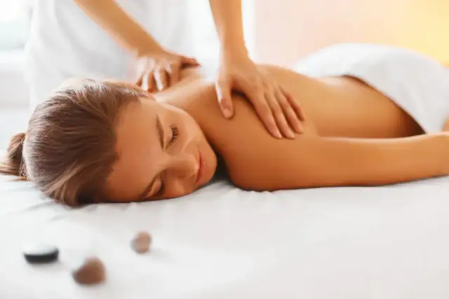 Kobieta leży na białym łóżku, a fizjoterapeuta masuje jej plecy.