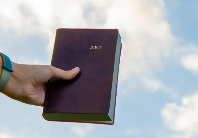 Dłoń trzyma Biblię na tle nieba. Czy to znaczy "Deus Deus Kosmateus"?