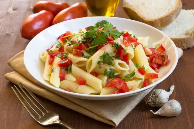 Świeży makaron penne z pomidorami i pietruszką, obok chleb, czosnek i oliwa. Porównanie makaronu świeżego z lodówki kontra suchego z paczki.