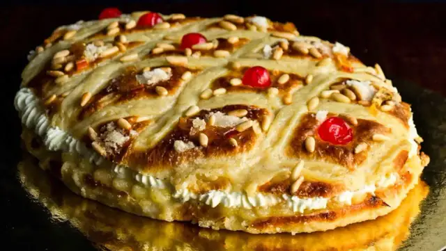 Deliciosa coca de San Juan rellena de crema, decorada con piñones, cerezas rojas y azúcar.
