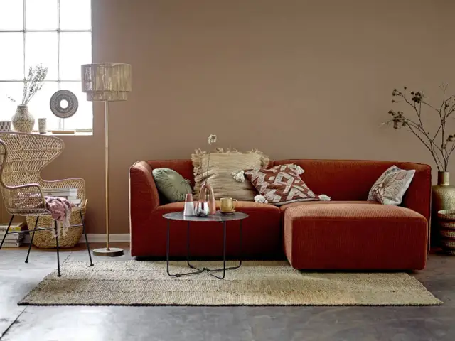 Przytulny salon w stylu boho. Pomarańczowa kanapa, wiklinowy fotel i dywan tworzą ciepłą paletę kolorów ziemi.