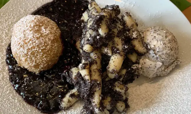 Gedrehte Nudeln mit Mohn, eine Kugel und Beerensoße, bestäubt mit Puderzucker.