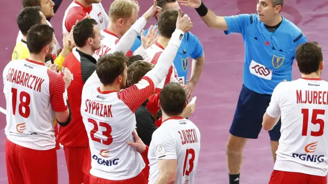 Polska kadra piłka ręczna świętuje zwycięstwo. Zawodnicy w białych strojach z czerwonymi detalami, z numerami 18, 23 i 15, cieszą się z sukcesu.