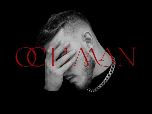 Krystian Ochman - nowa płyta. Artysta z dłonią na twarzy, w tle czerwony napis "OCHMAN".