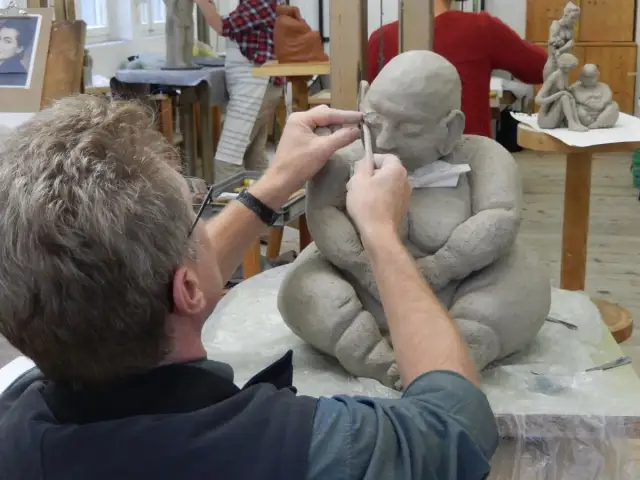 Ein Künstler formt mit Werkzeug eine Tonfigur in einem Atelier.