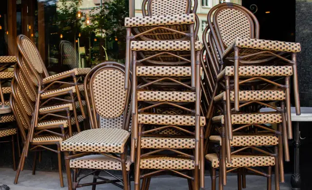 Gestapelte braune Bistrostühle mit geflochtenen Sitzflächen und Rückenlehnen vor einem Restaurant.