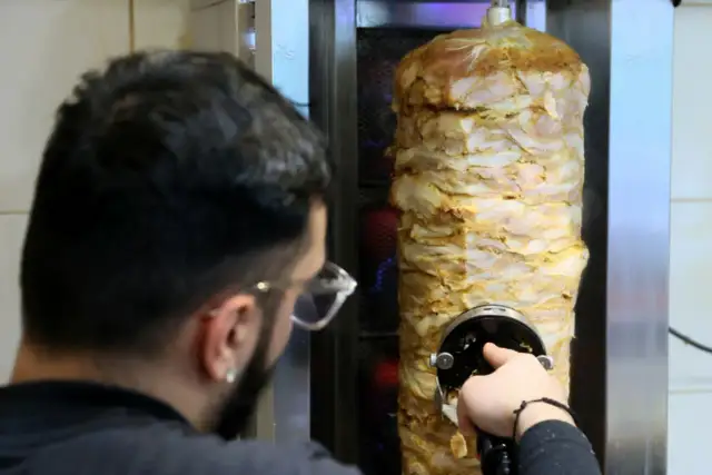 Mężczyzna kroi mięso z pionowego rożna na kebab.