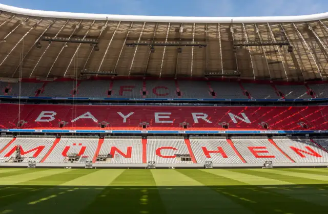Puste trybuny Allianz Arena z napisem "BAYERN MÜNCHEN" w czerwonych i białych siedzeniach.