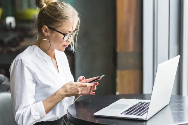 Kobieta w okularach i białej koszuli korzysta z telefonu, obok leży laptop. Upewnij się, że Twoje datezone połączenie nie jest prywatne.
