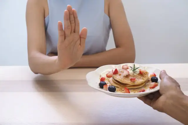 Dłoń odrzuca talerz z naleśnikami i owocami. To symboliczne przedstawienie, jak dieta 1200 kcal efekty po 2 tygodniach motywuje do zdrowych wyborów.