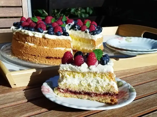Prosty tort biszkoptowy z kremem i owocami leśnymi, udekorowany malinami i borówkami.
