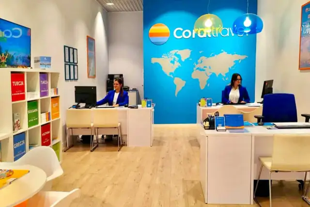 Biuro podróży Coral Travel z pracownicami za ladą i mapą świata na ścianie.