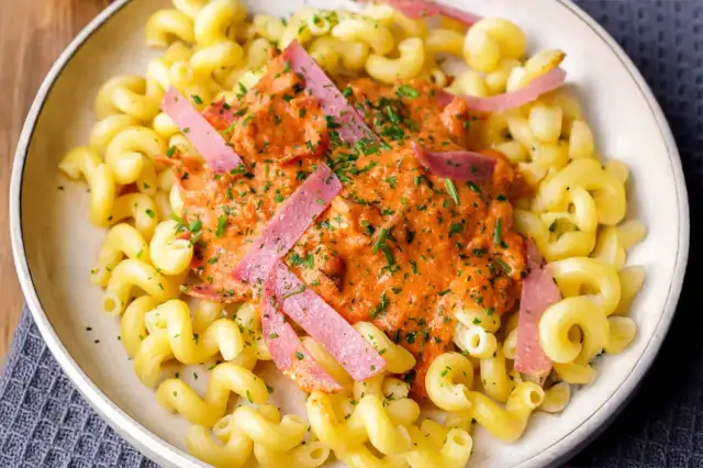 Gedrehte Nudeln mit cremiger Tomatensoße und rosa Wurststreifen, garniert mit Petersilie.