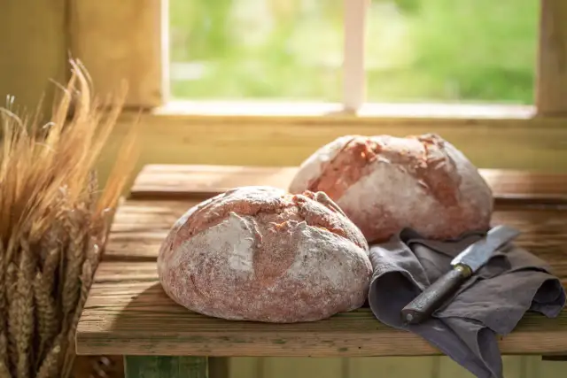 Dos panes rústicos, un cuchillo y espigas de trigo, evocando cómo se hace el pan artesanalmente.