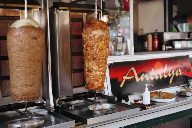 Dwa pionowe rożna z mięsem do kebaba na tle budki z napisem "Antalya".