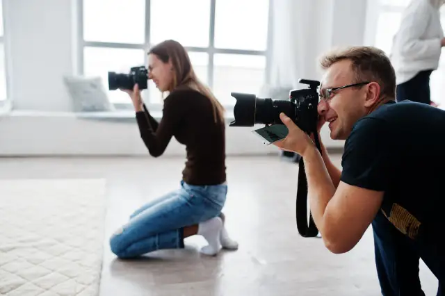 Dwóch fotografów klęczy i robi zdjęcia aparatem w jasnym studiu.