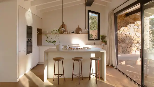 Cocina luminosa con isla central, taburetes y vistas a un patio de piedra, ideal para casas de campo modernas.