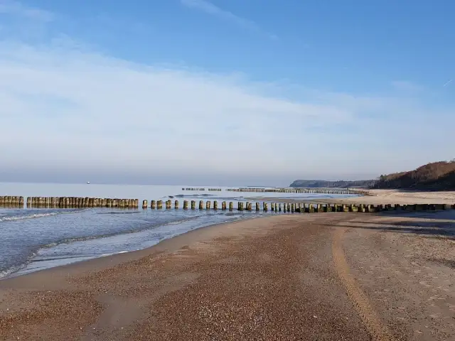 Spokojne morze i pusta plaża w Rusinowie nad morzem. Drewniane falochrony wcinają się w wodę, tworząc malowniczy krajobraz.