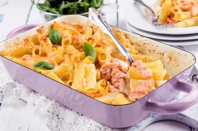 Zapiekanka z makaronem i łososiem w fioletowym naczyniu, udekorowana bazylią.