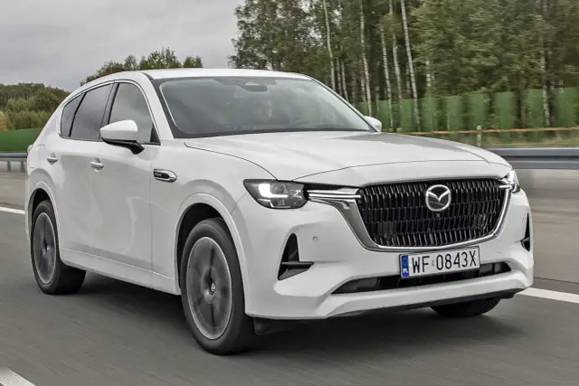 Biała Mazda CX-60 jedzie po drodze, otoczona drzewami. Sprawdź, jaka jest mazda cx 60 cena i wyposażenie.