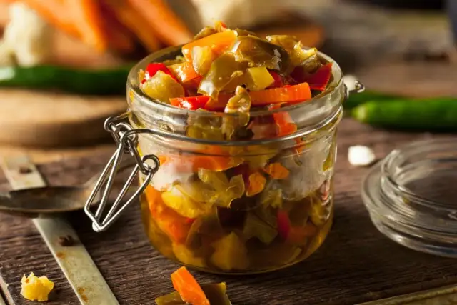 Un frasco de vidrio lleno de escabeche de verduras, con trozos de pimientos y zanahorias.
