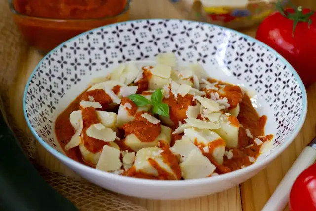 Gnocchi ziemniaczane w sosie pomidorowym, posypane parmezanem. Obok pomidor i cukinia.