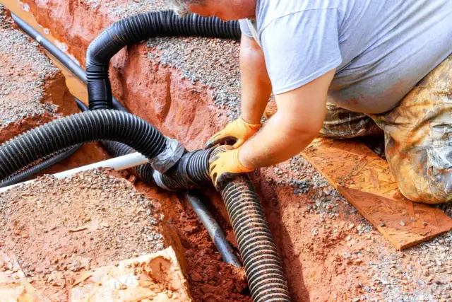 Instalator łączy rury odprowadzające wodę do budowanej studni chłonnej.