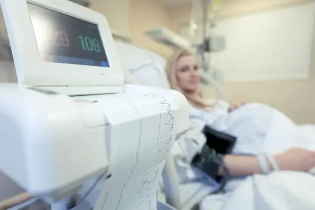 Monitor KTG z wydrukiem zapisu i ciężarną w tle.