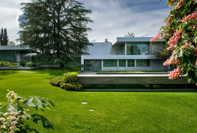 Casa moderna rodeada de jardines bonitos, césped verde y flores rosadas.