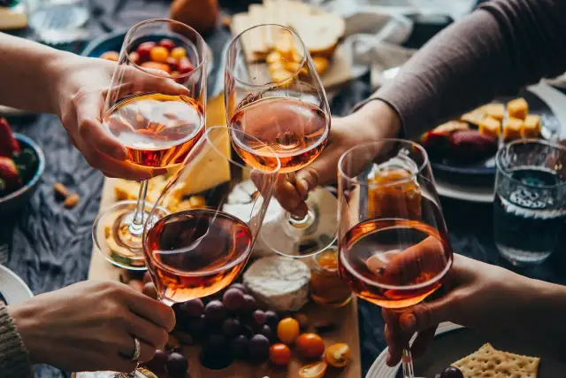 Różowe wino, czyli alkohol etylowy w jedzeniu, w kieliszkach na tle serów, owoców i przekąsek.