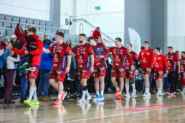 Drużyna kwidzyn piłka ręczna w czerwonych strojach wchodzi na halę, pozdrawiając kibiców.