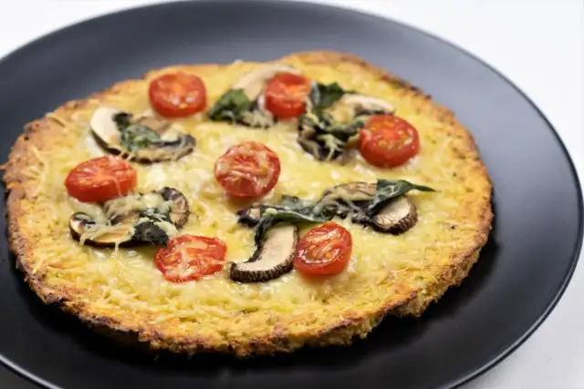 Deliciosa pizza de coliflor con queso derretido, champiñones y tomates cherry.